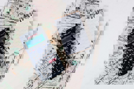 An image of a calculator and a paper on top of dollar bills