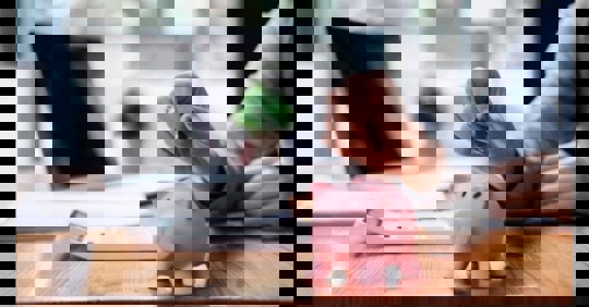 A hand drops a coin into a pink piggy bank.