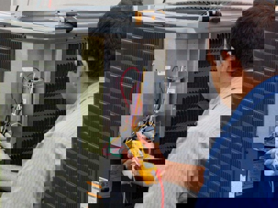 An HVAC technician is using a multimeter to troubleshoot an air conditioning unit.