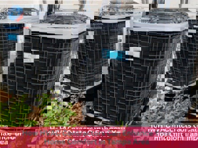 Two outdoor AC units sit on concrete pads, partially obscured by small bushes.