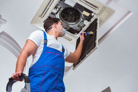 A technician wearing a mask cleans the air conditioning unit.