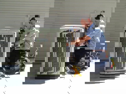 A technician kneels, servicing a Trane air conditioner unit outside a building.