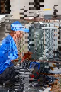 n HVAC technician servicing an outdoor air conditioning unit.