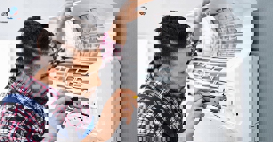 A technician in a plaid shirt repairs a mini split AC unit.