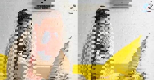 A person feeling unwell is shown wrapped in a blanket, using a tissue to blow their nose.