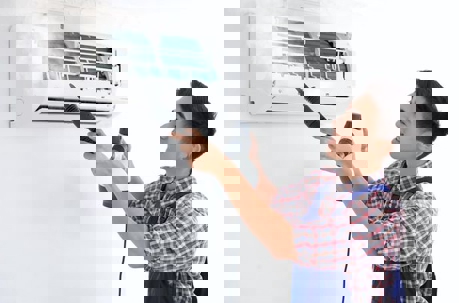 A technician cleans an air conditioning unit with a power washer.