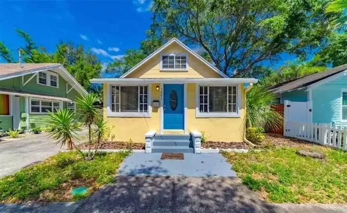 Charming yellow home with blue door, flanked by greenery.