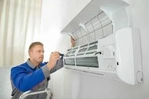 An HVAC specialist inspects the filters of a wall-mounted air conditioner.