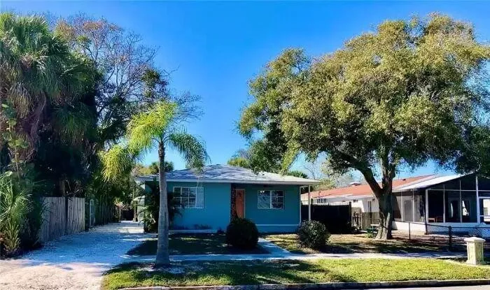 The blue house is surrounded by green trees and landscaping. 