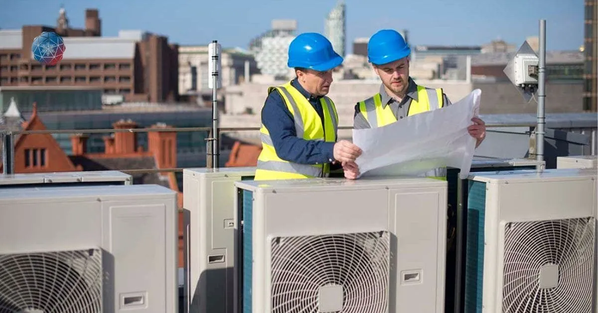 Two HVAC technicians in hard hats review plans atop a building's rooftop HVAC system.