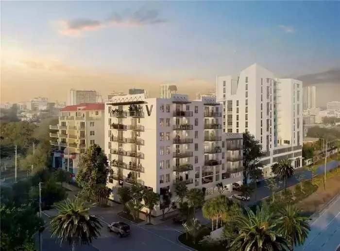A sunny, aerial view of a white condominium complex in an urban setting.